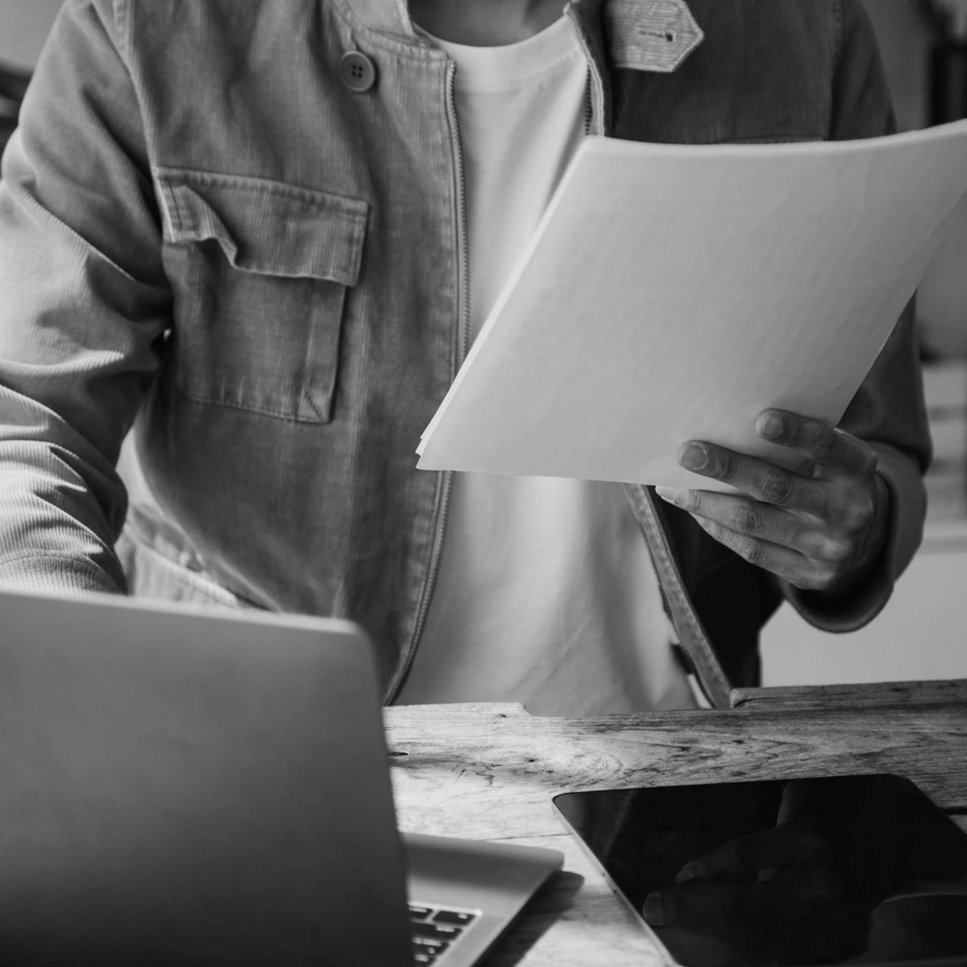 a person holds a paper up in front of them as if they're reading it as their other hand rests on a computer keyboard