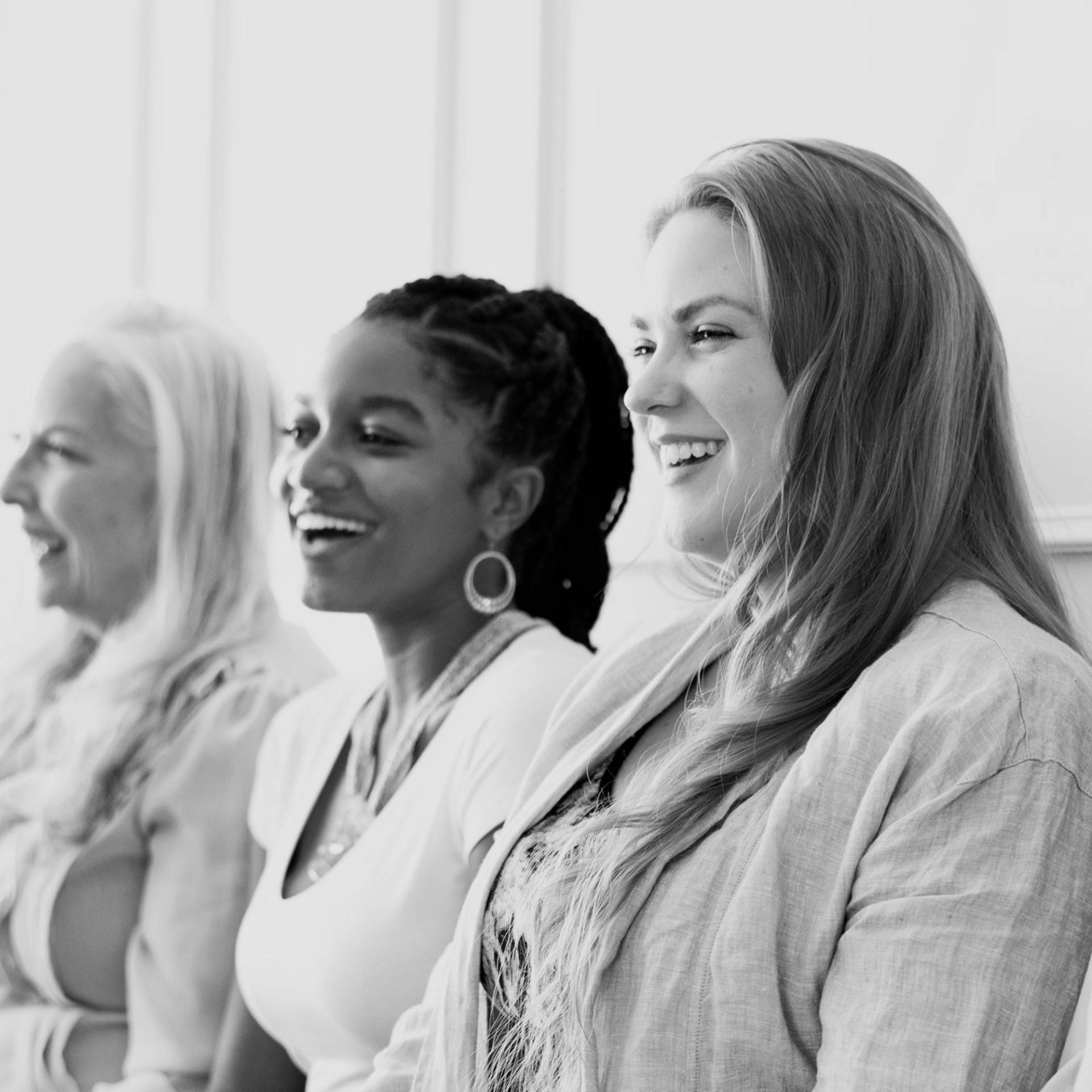 three diverse women stand side by side, smiling and laughing as they look at something out of view