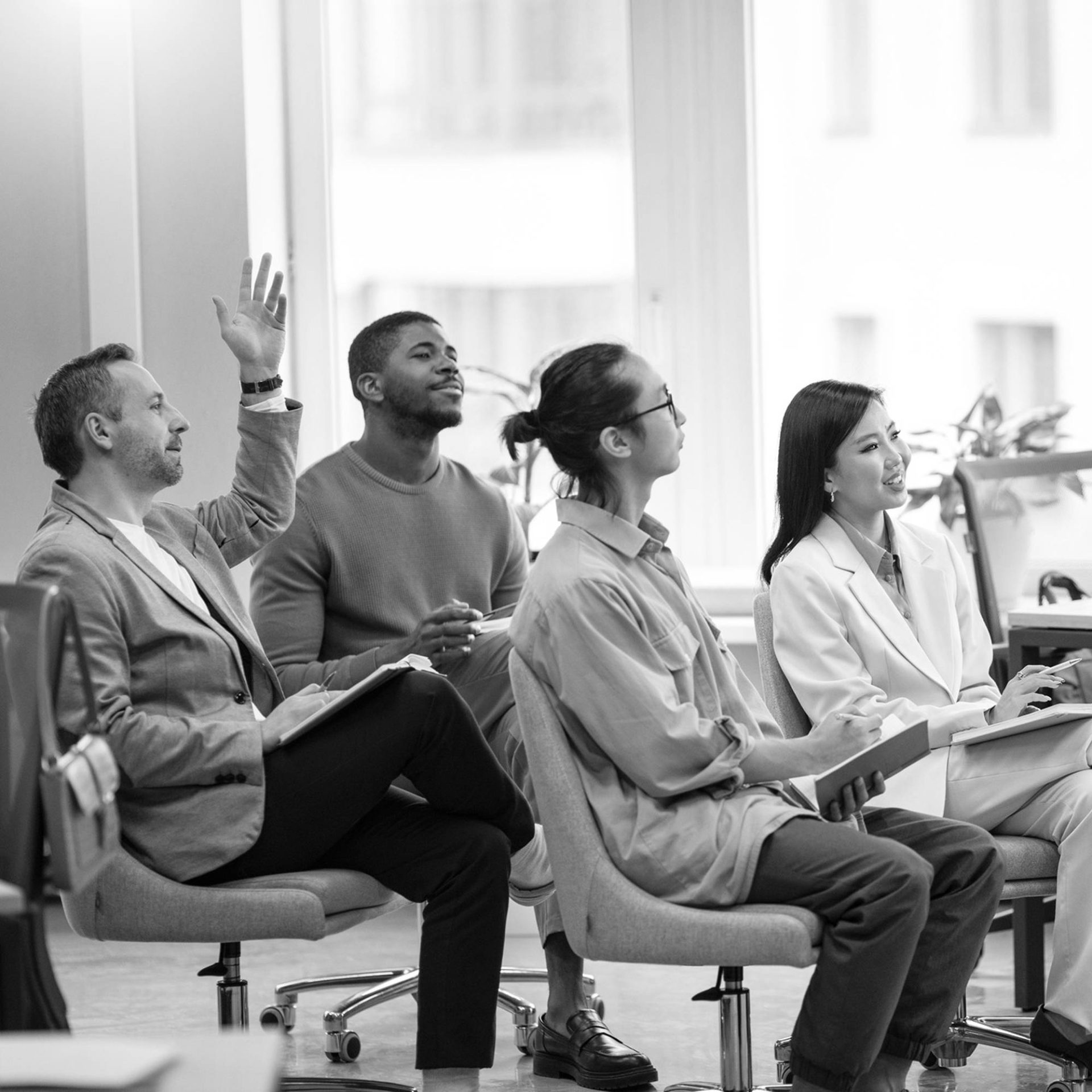 several people sit in chairs facing the same direction as one person raises their hand as if they have a question for a speaker who is out of view