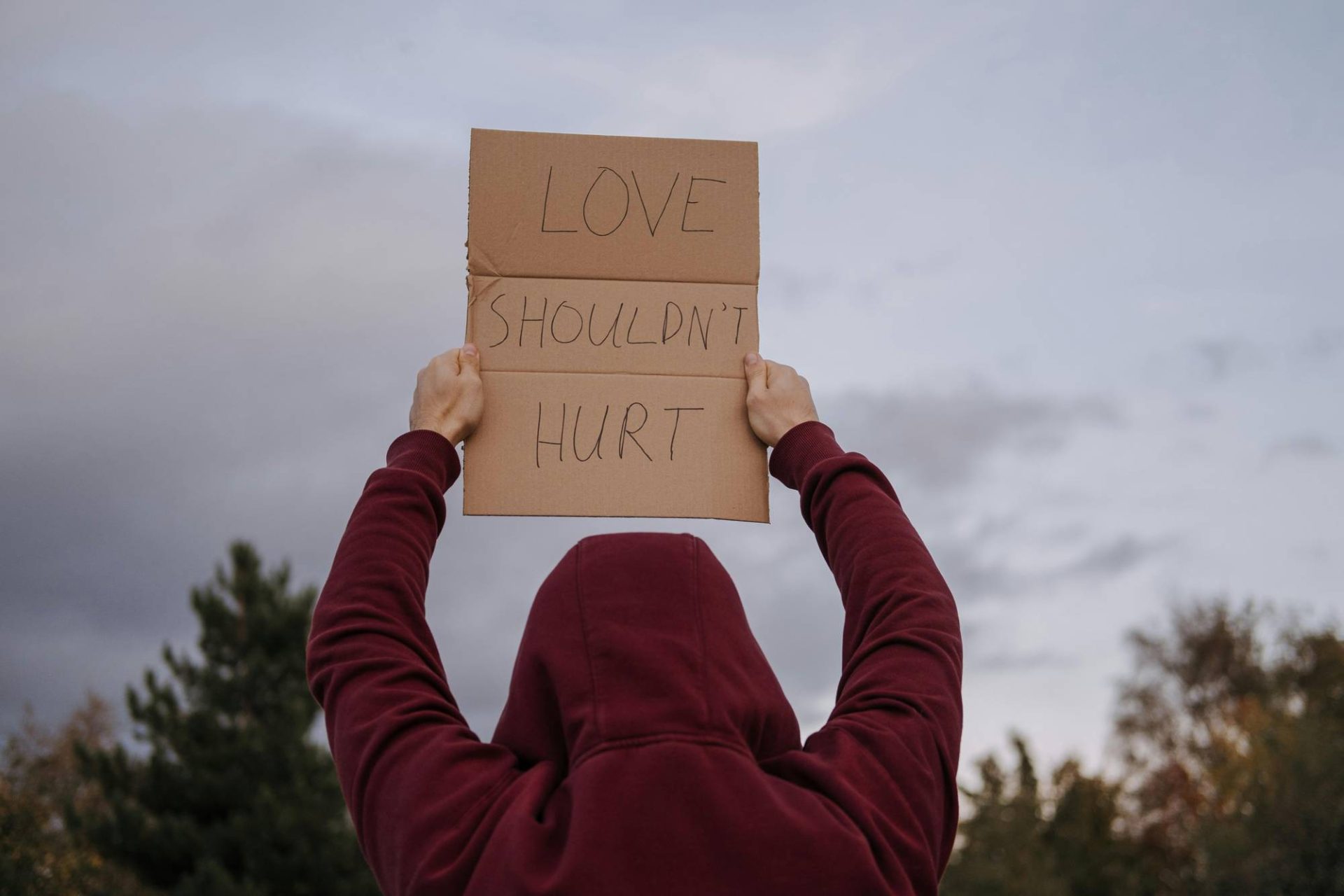a person holds a cardboard sign that says "love shouldn't hurt"