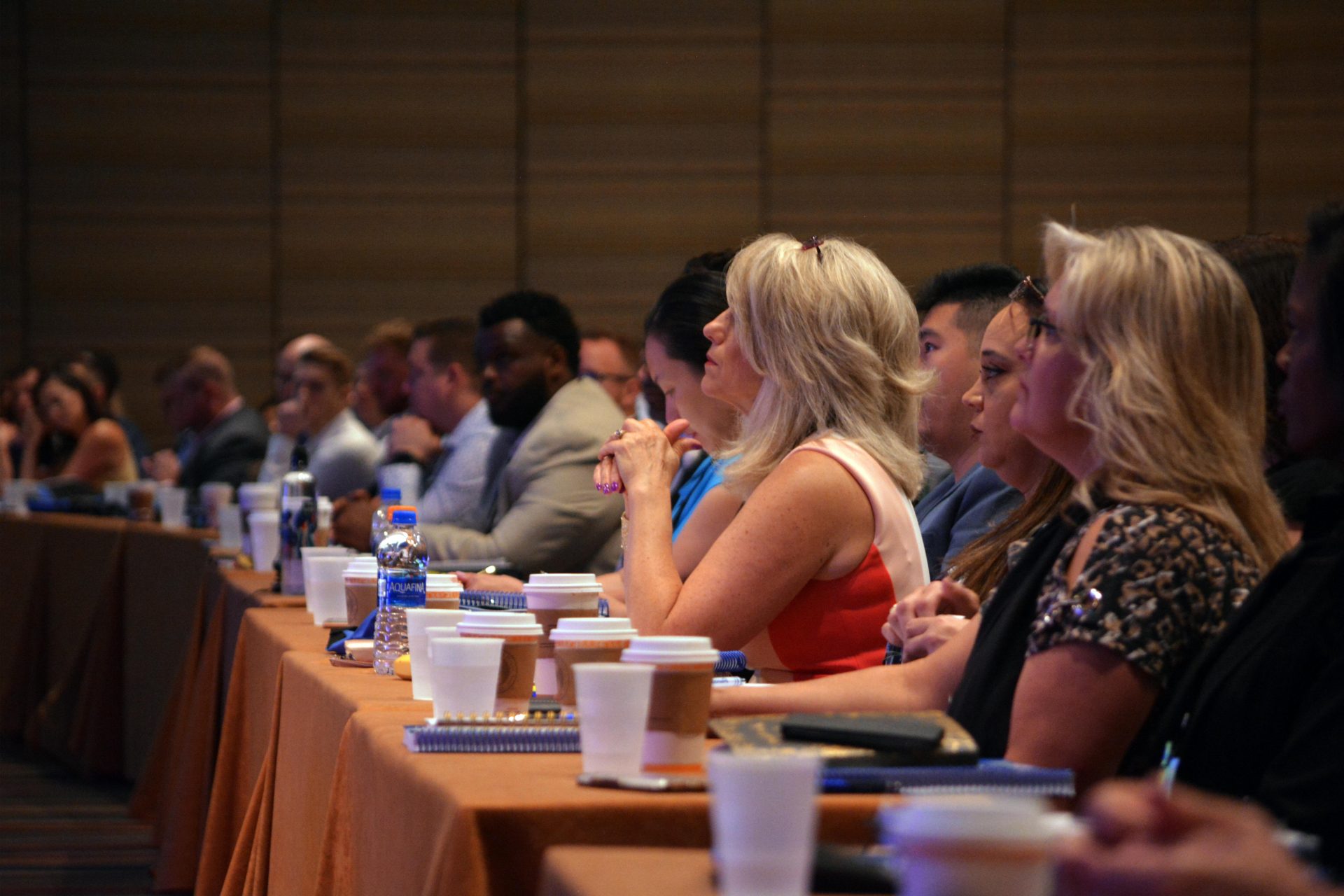 a diverse crowd looks towards the front of a room as they appear to listen to a speaker