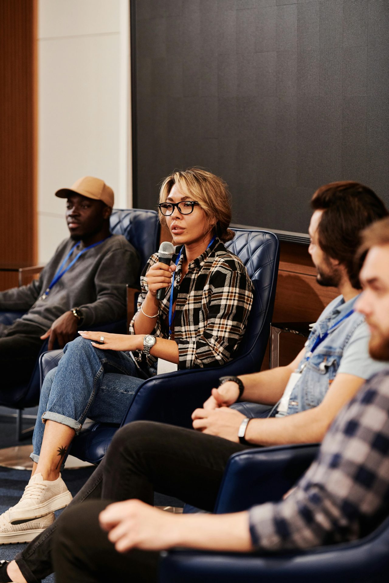 a serious-looking middle-age woman speaks into a microphone as she sits among other middle-age people