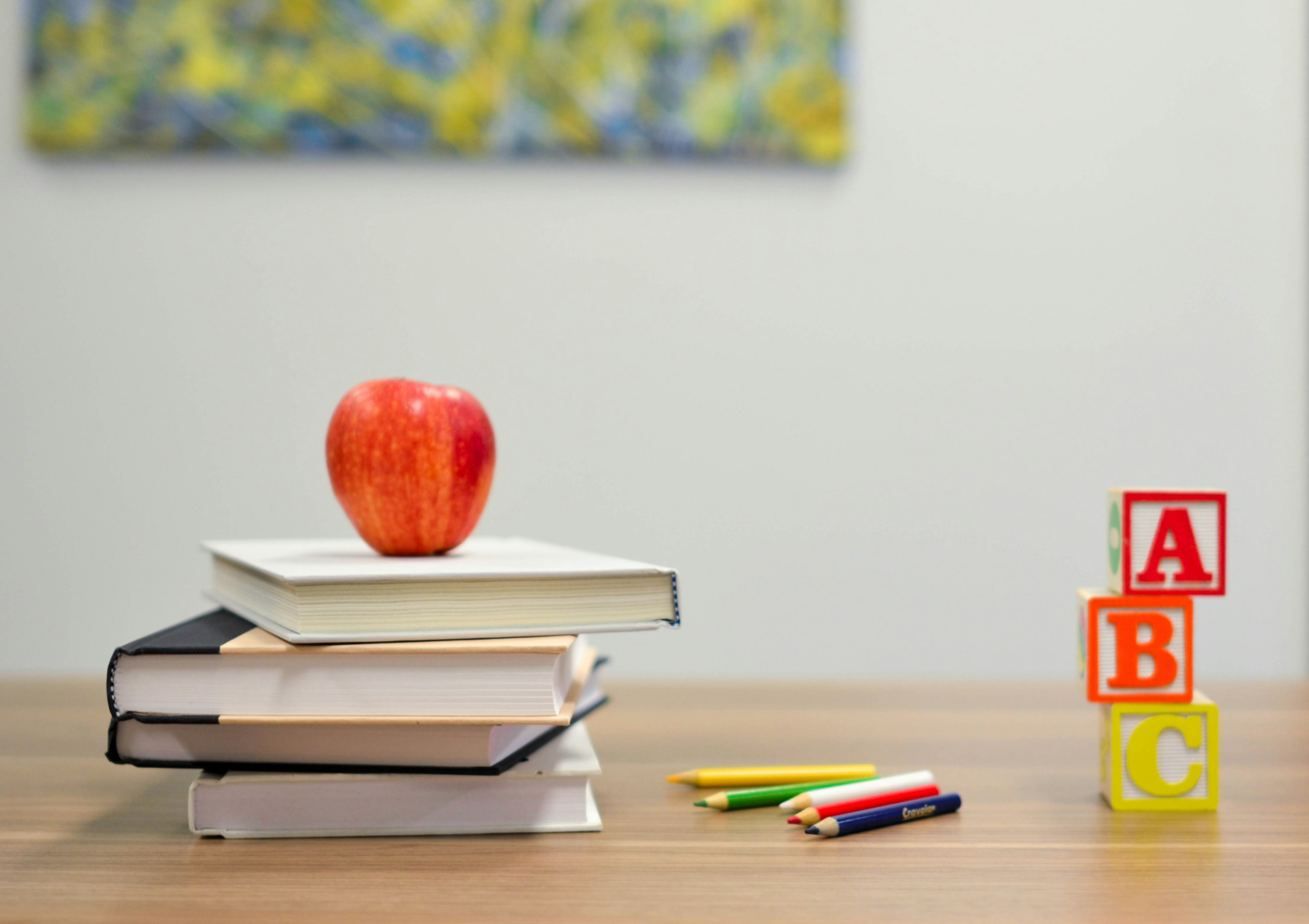 an apple sits atop a stack of school books next to writing utensils and ABC blocks